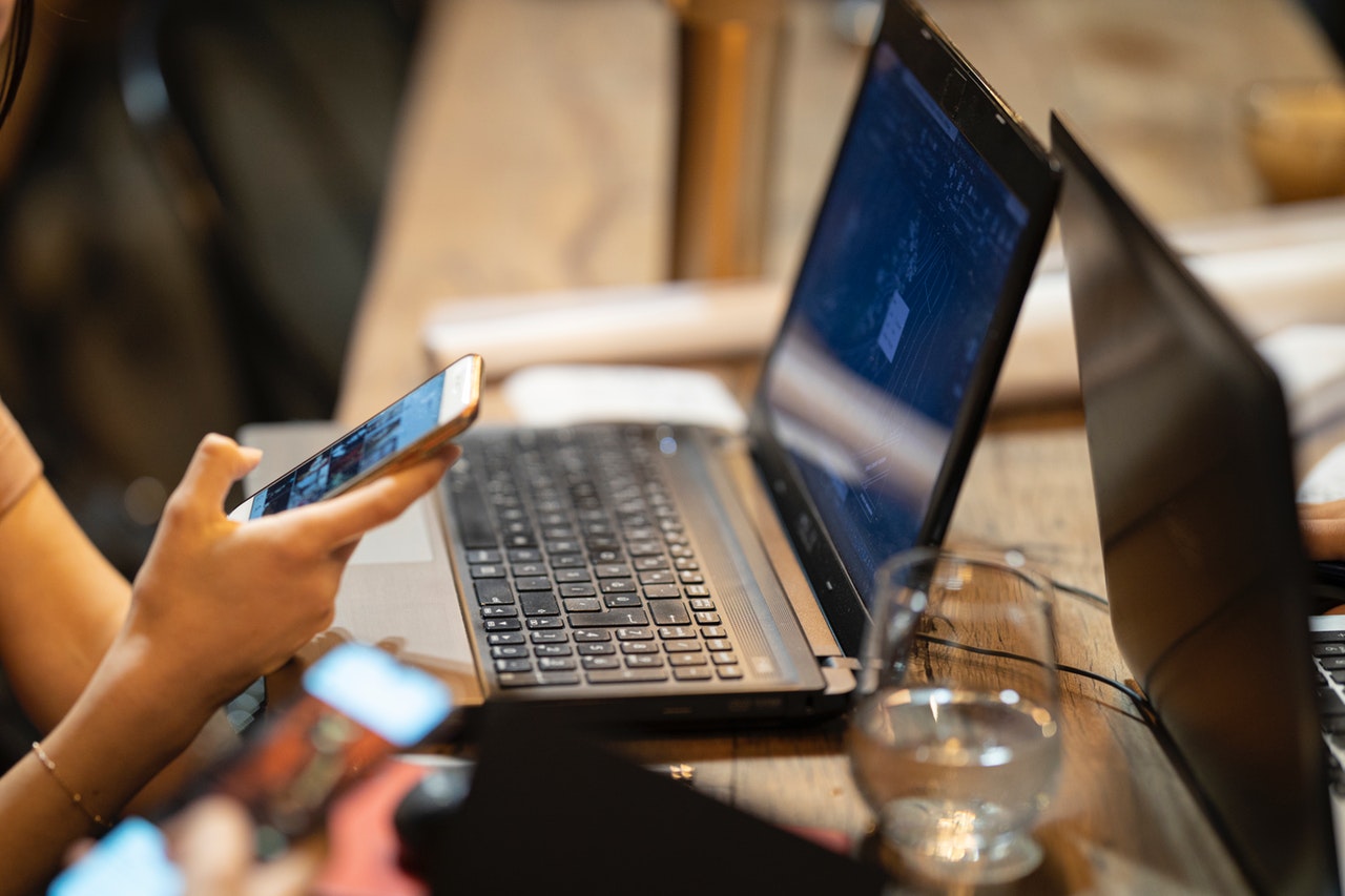 Person using smartphone while working on laptop, illustrating the importance of technology in personal reputation